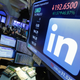 The LinkedIn logo at the New York stock exchange on a monitor with people walking by.